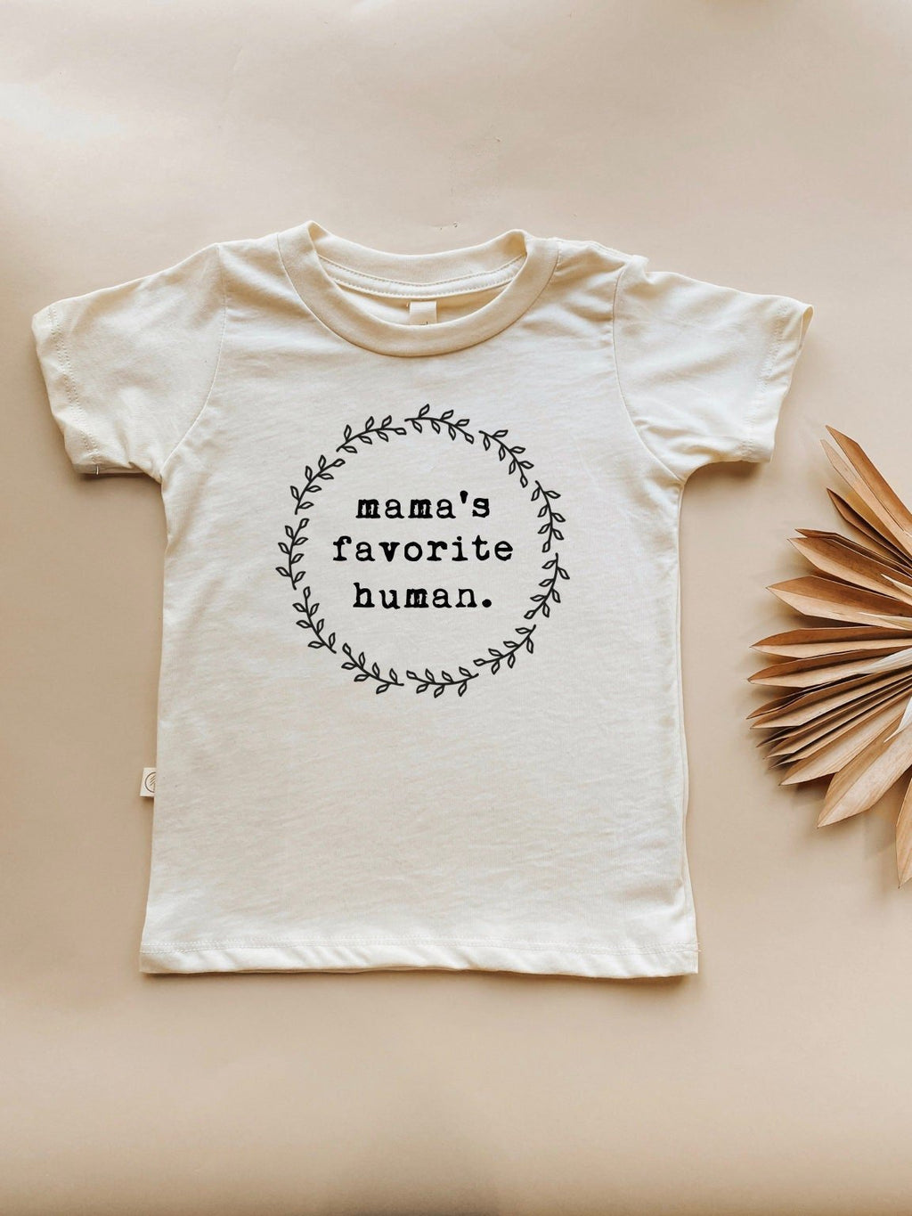 White t-shirt with 'mama's favorite human' text on a beige background