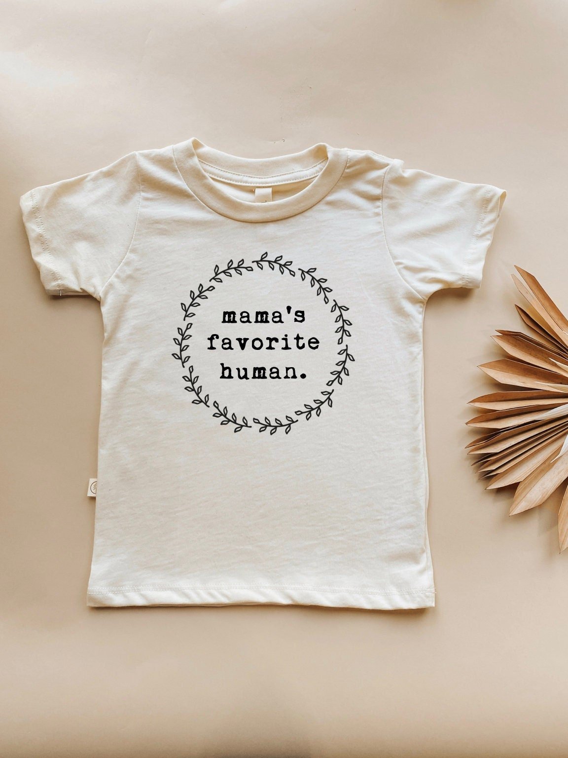 White t-shirt with 'mama's favorite human' text on a beige background