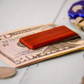 Wooden money clip on a stack of dollar bills with coins and keys in the background.