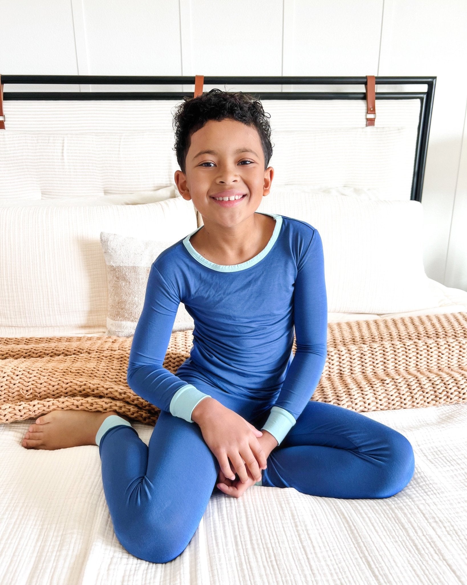 Child wearing blue pajamas sitting on a bed.