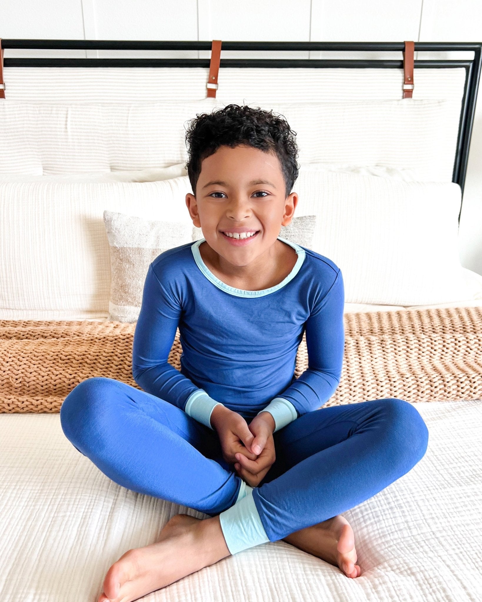 Child wearing blue pajamas sitting on a bed.