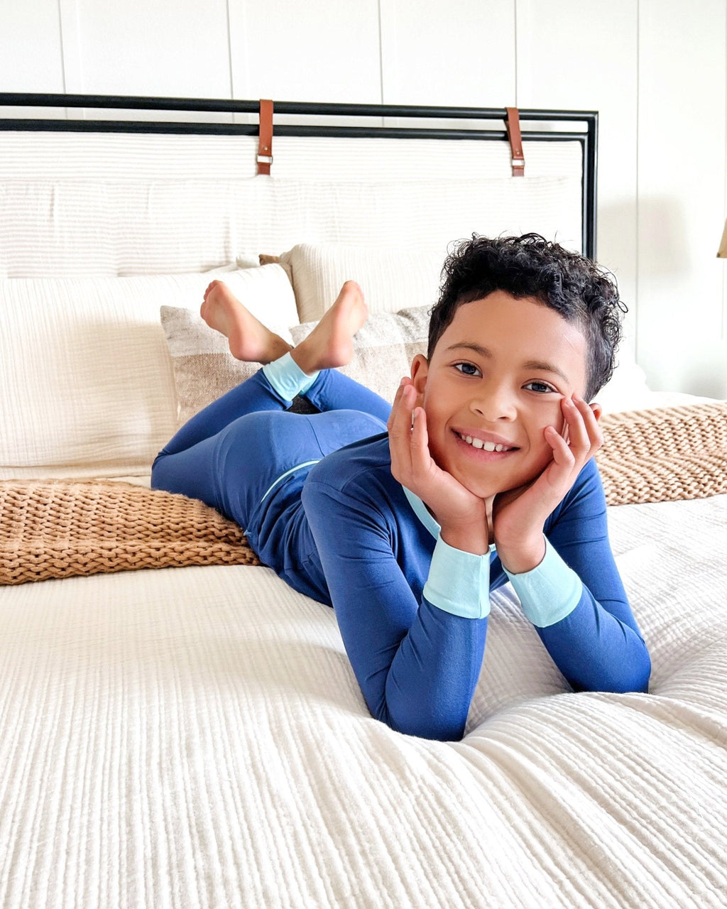Child in blue pajamas lying on a bed with a white background