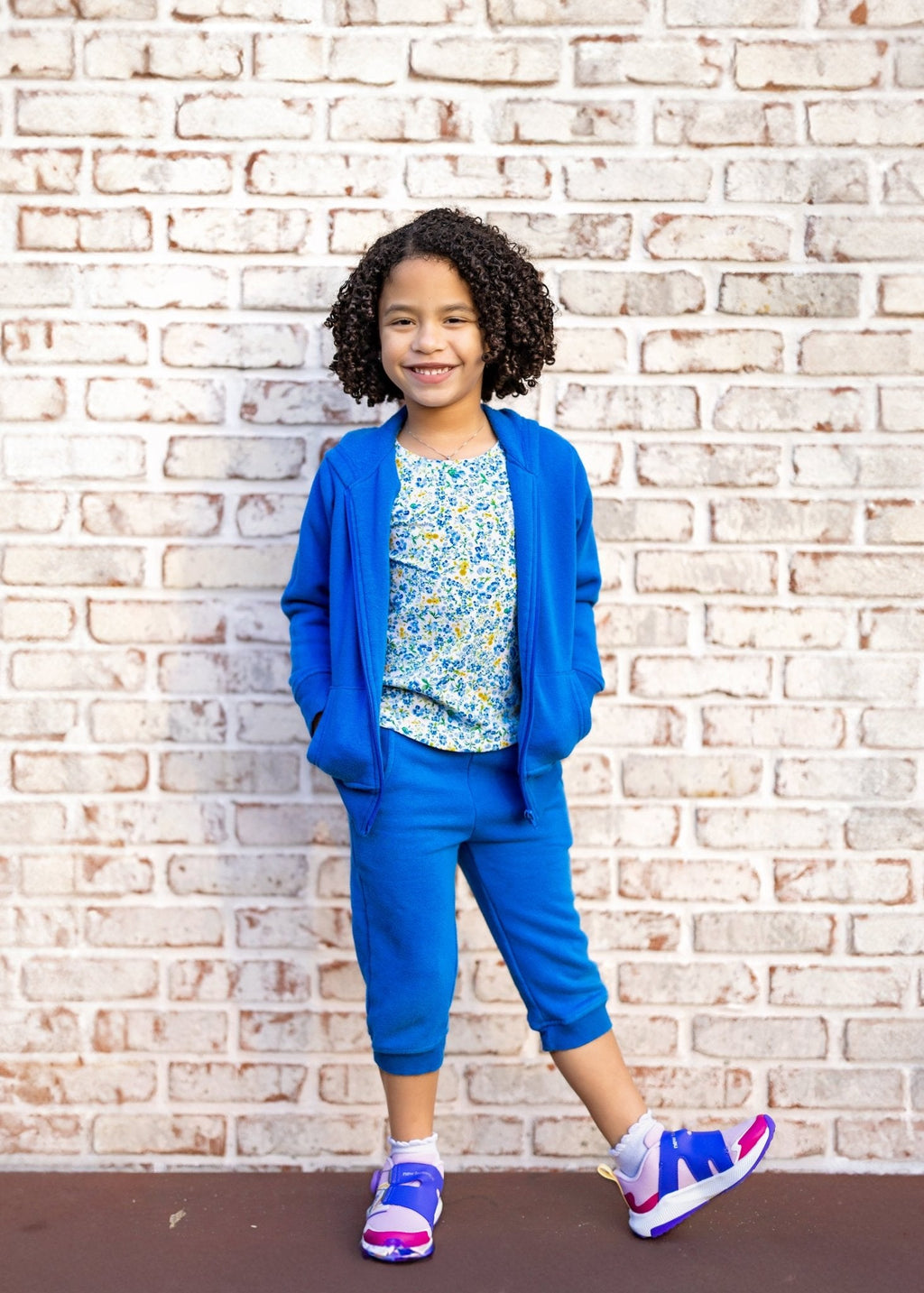 Child wearing a blue outfit with a floral top against a brick wall