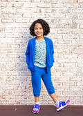Child wearing a blue outfit with a floral top against a brick wall