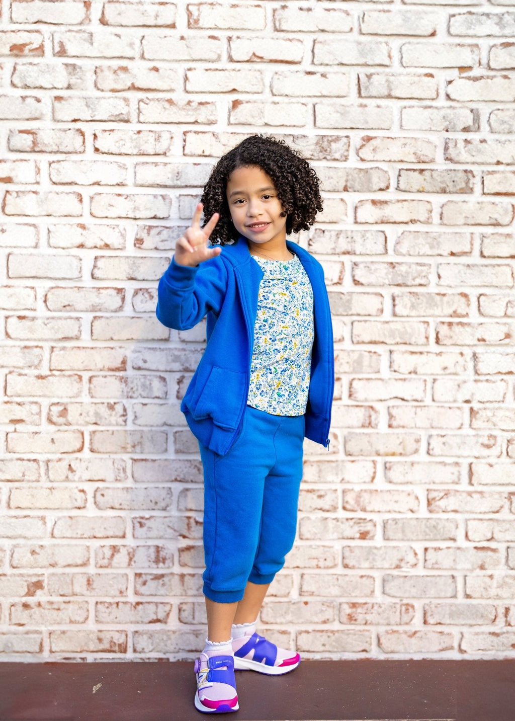 Child in a blue outfit standing against a brick wall