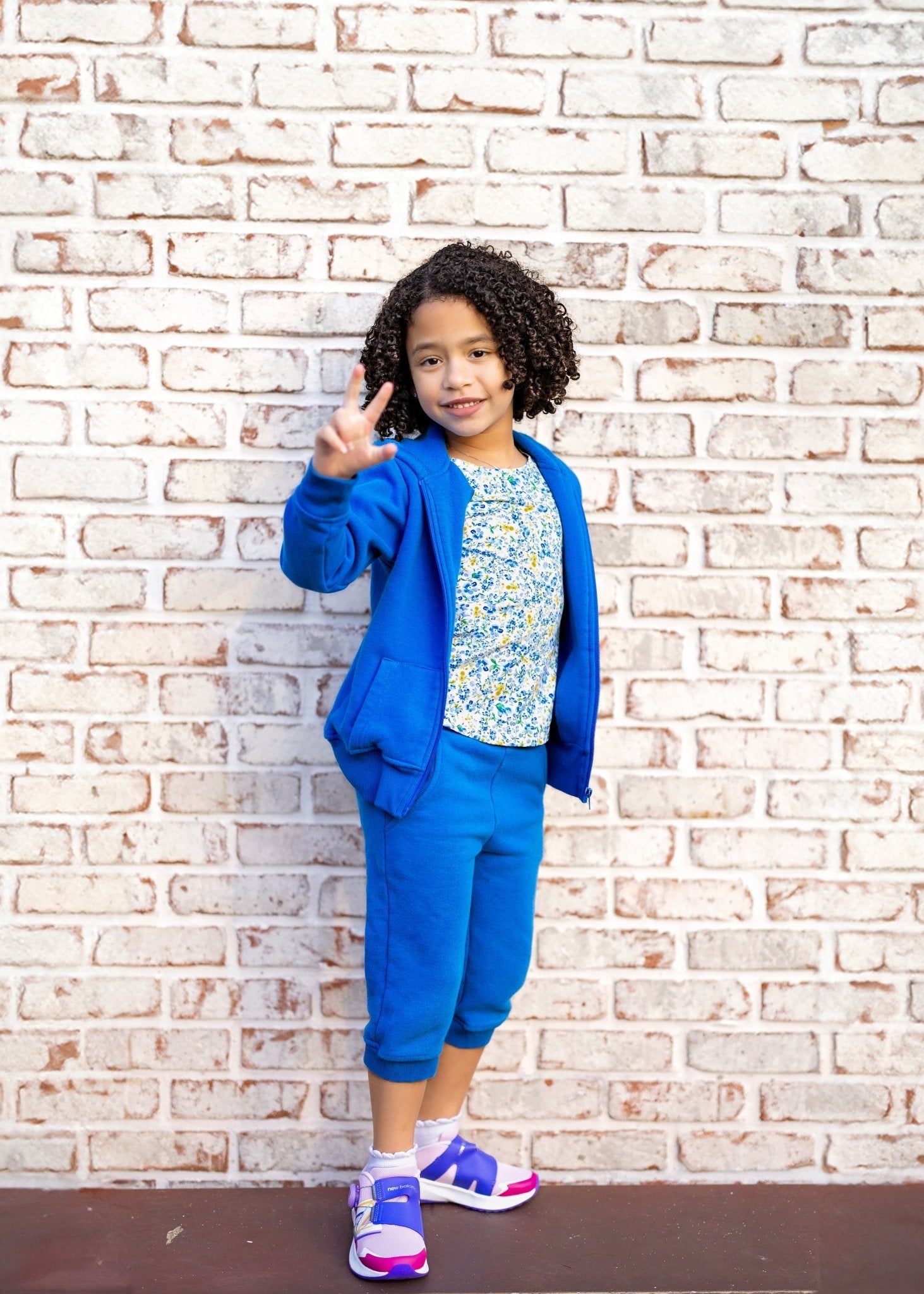 Child in a blue outfit standing against a brick wall