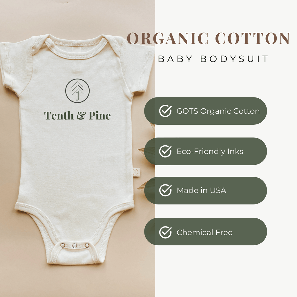 Organic cotton baby onesie with Tenth & Pine branding on a beige background