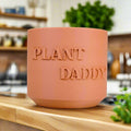 Terracotta-colored pot with 'Plant Daddy' text on a kitchen counter