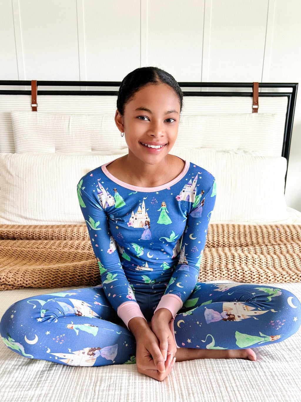 Young girl wearing blue pajamas with castle design sitting on a bed.