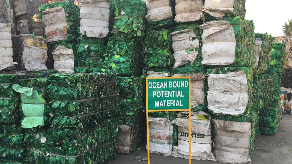 Stacks of green and white plastic materials with a sign indicating 'Ocean Bound Potential Material' in an outdoor setting.