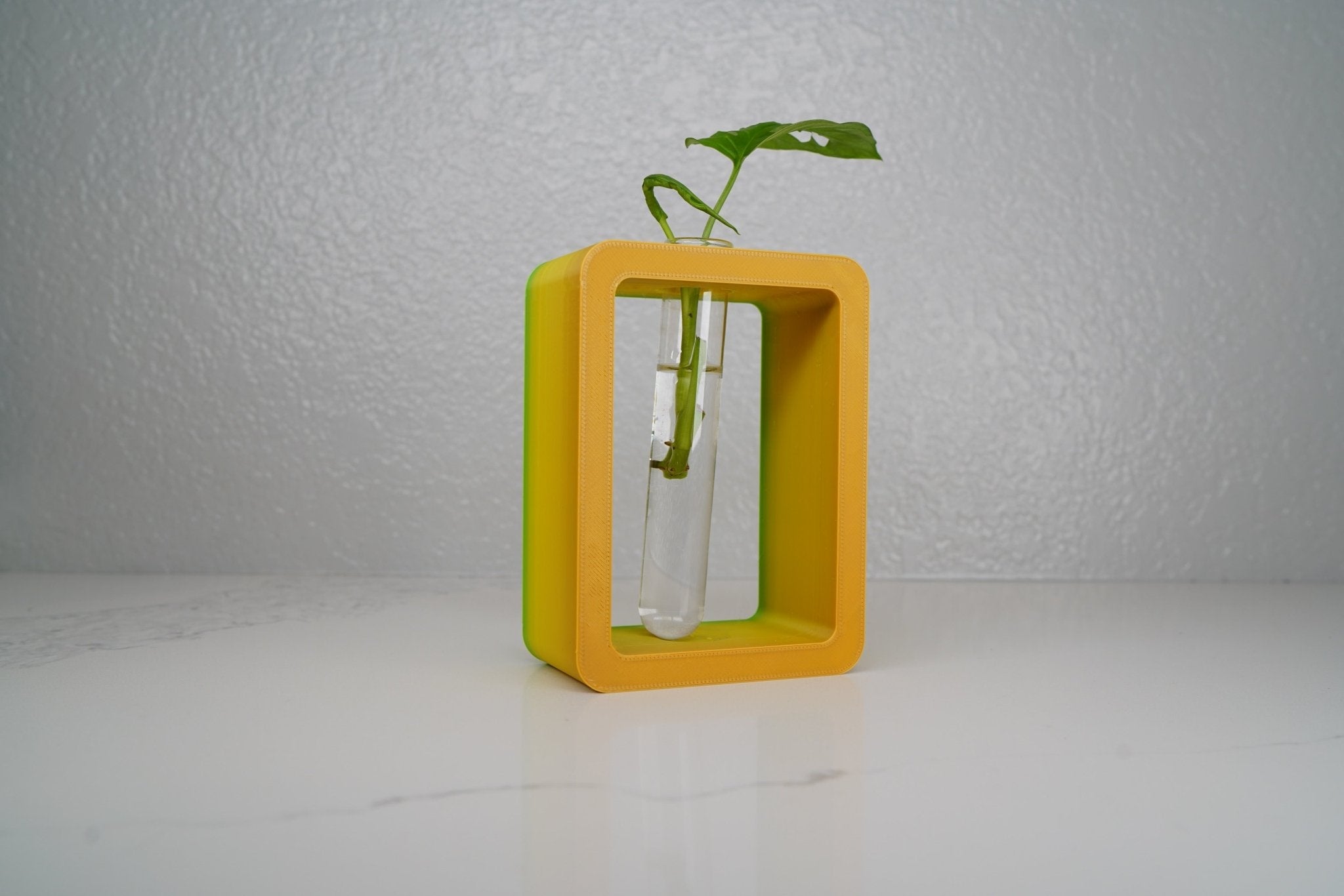 Yellow cube-shaped vase with a plant on a white surface and light gray background