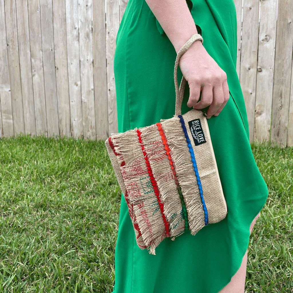 Person holding a colorful striped bag with a wooden fence and grass in the background