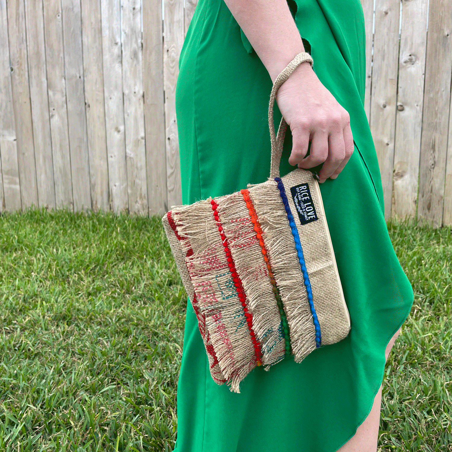 Person holding a colorful striped bag with a wooden fence and grass in the background