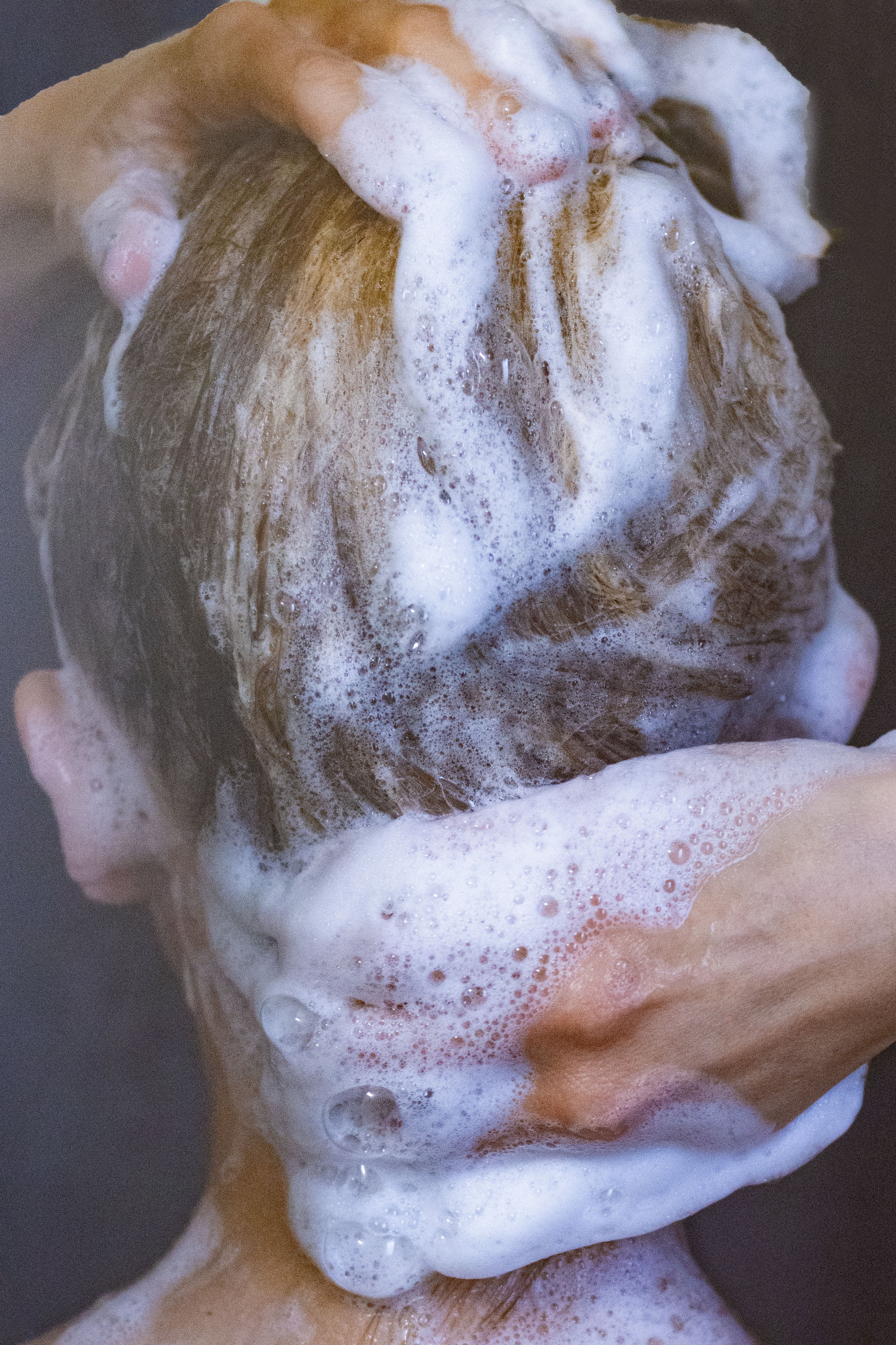 Person washing their hair with soapy hands and lather.