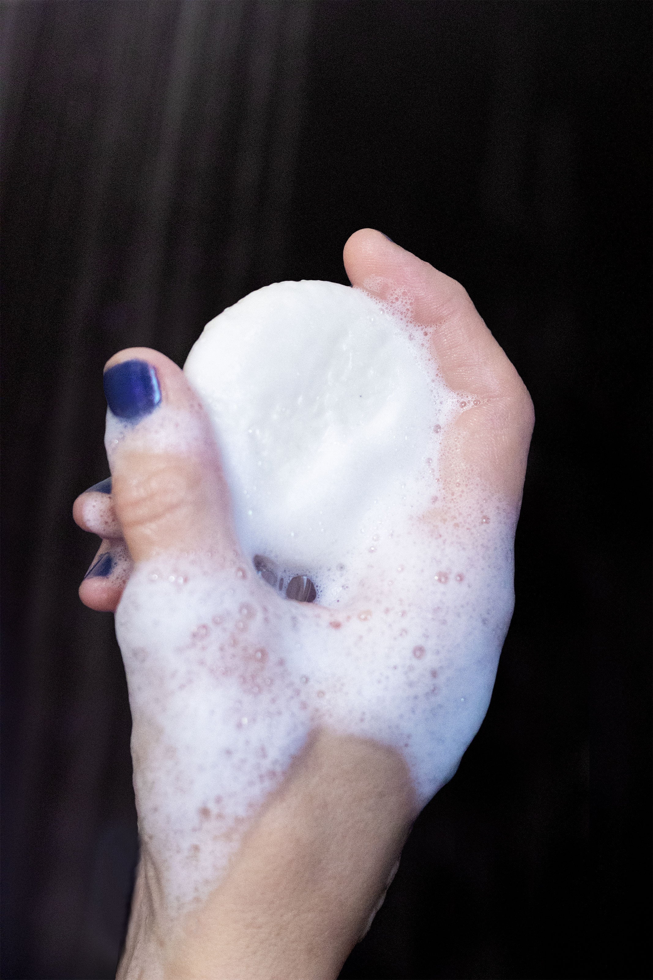 Hand holding a foamy shampoo bar against a dark background