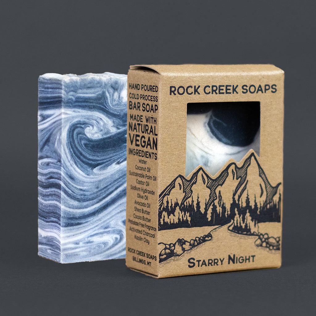 Marble-patterned bar of soap next to its packaging with 'Rock Creek Soaps' branding on a dark background.