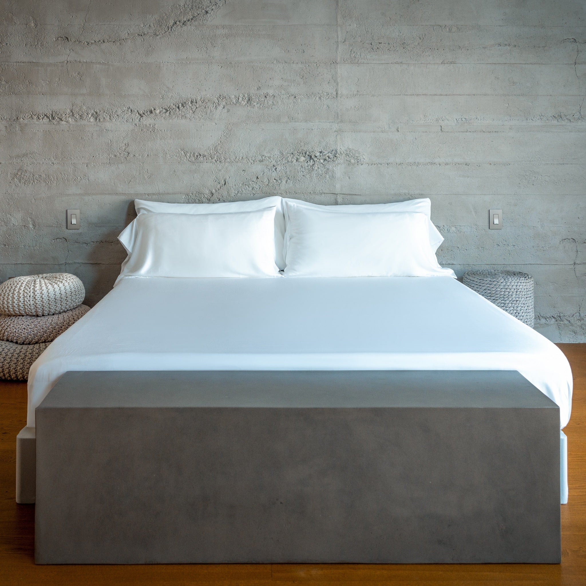Bed with white bedding and gray box  against a concrete wall.