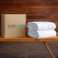 Stack of white towels next to a cardboard box with 'bathméd' branding on a wooden surface.