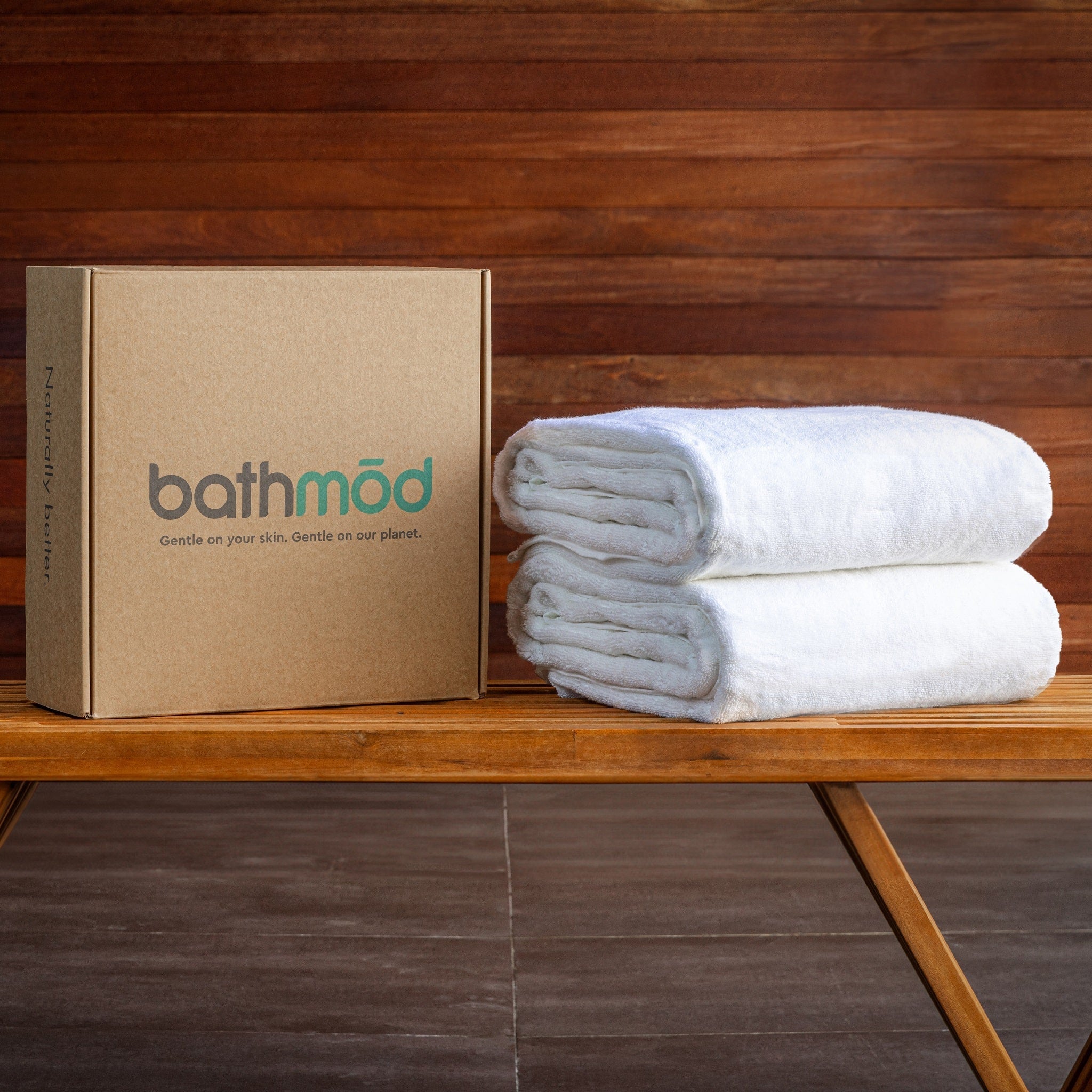 Stack of white towels next to a cardboard box with 'bathméd' branding on a wooden surface.