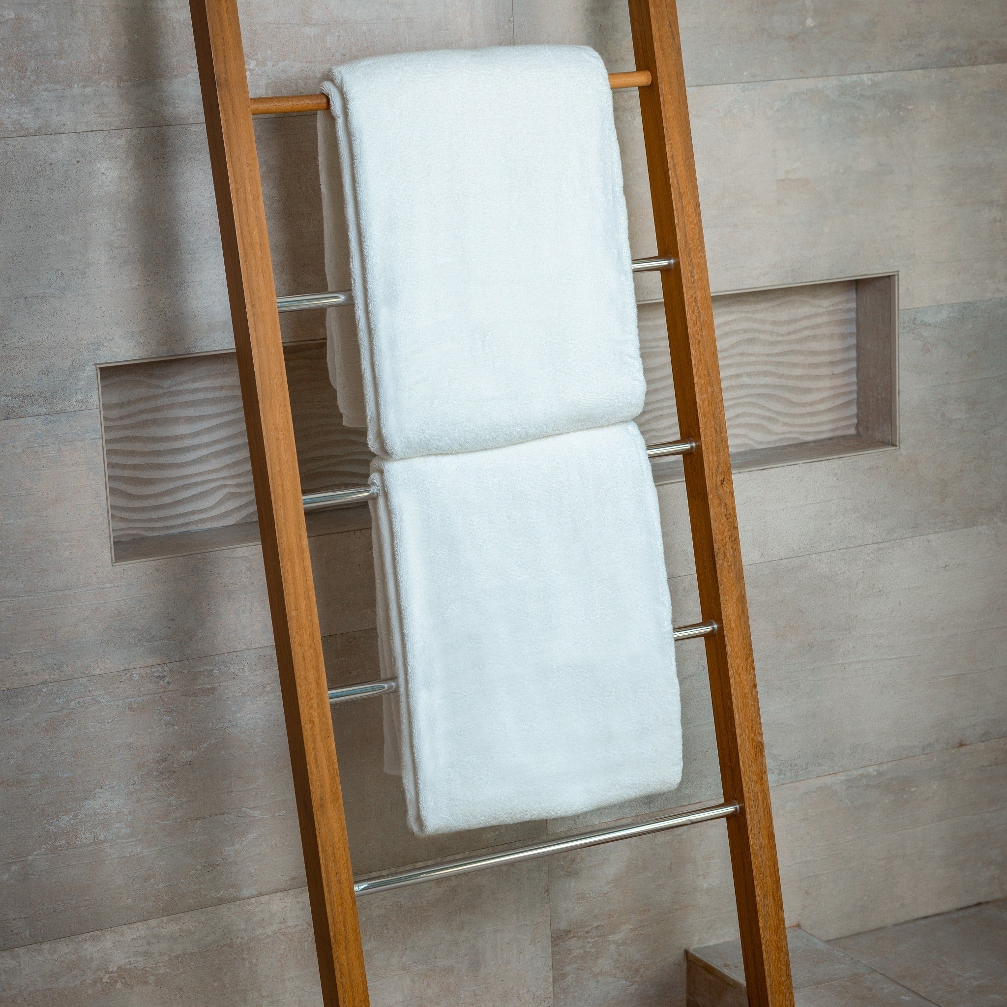 Wooden towel ladder with white towels against a tiled bathroom wall.