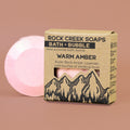 Pink bath bomb next to its cardboard packaging on a brown background
