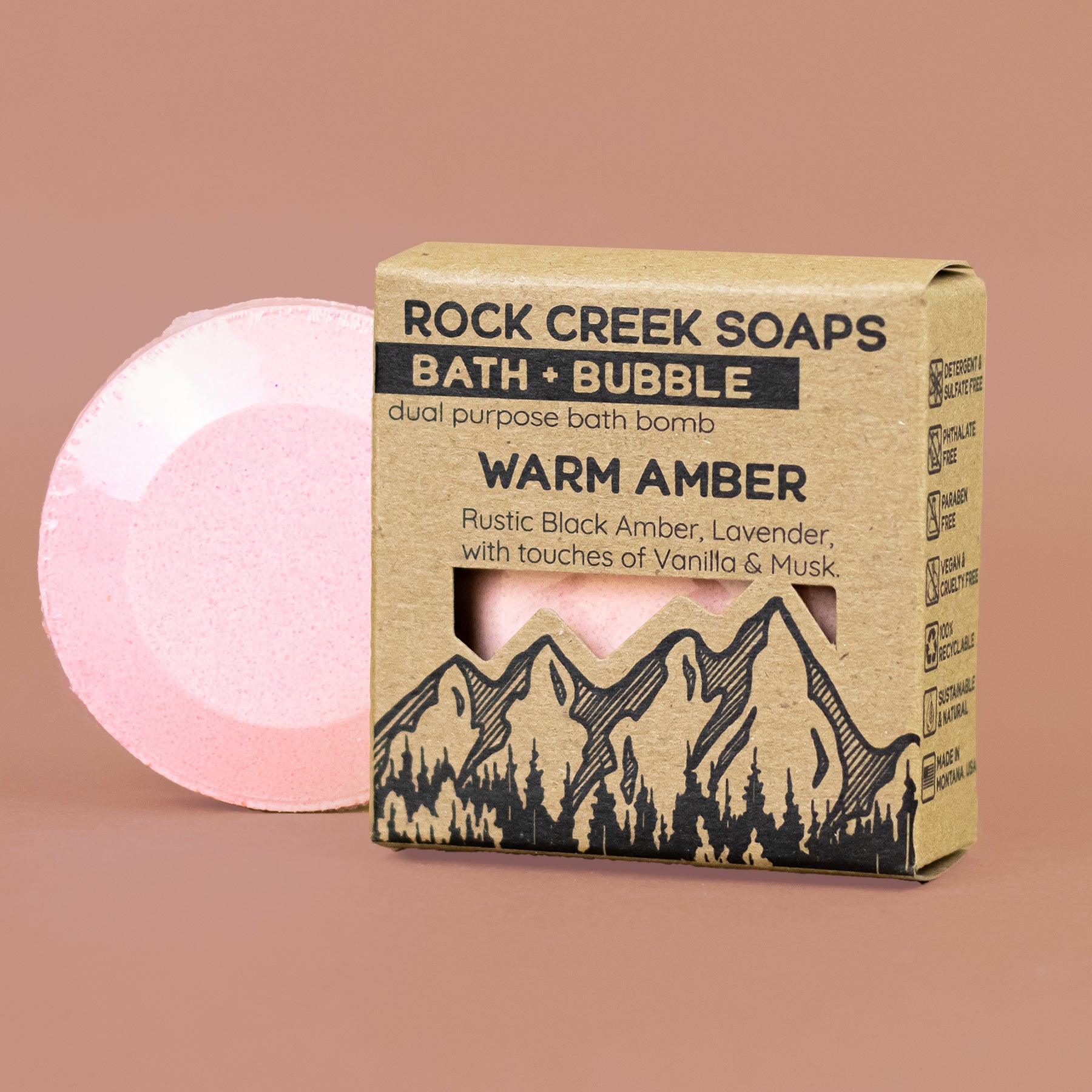 Pink bath bomb next to its cardboard packaging on a brown background