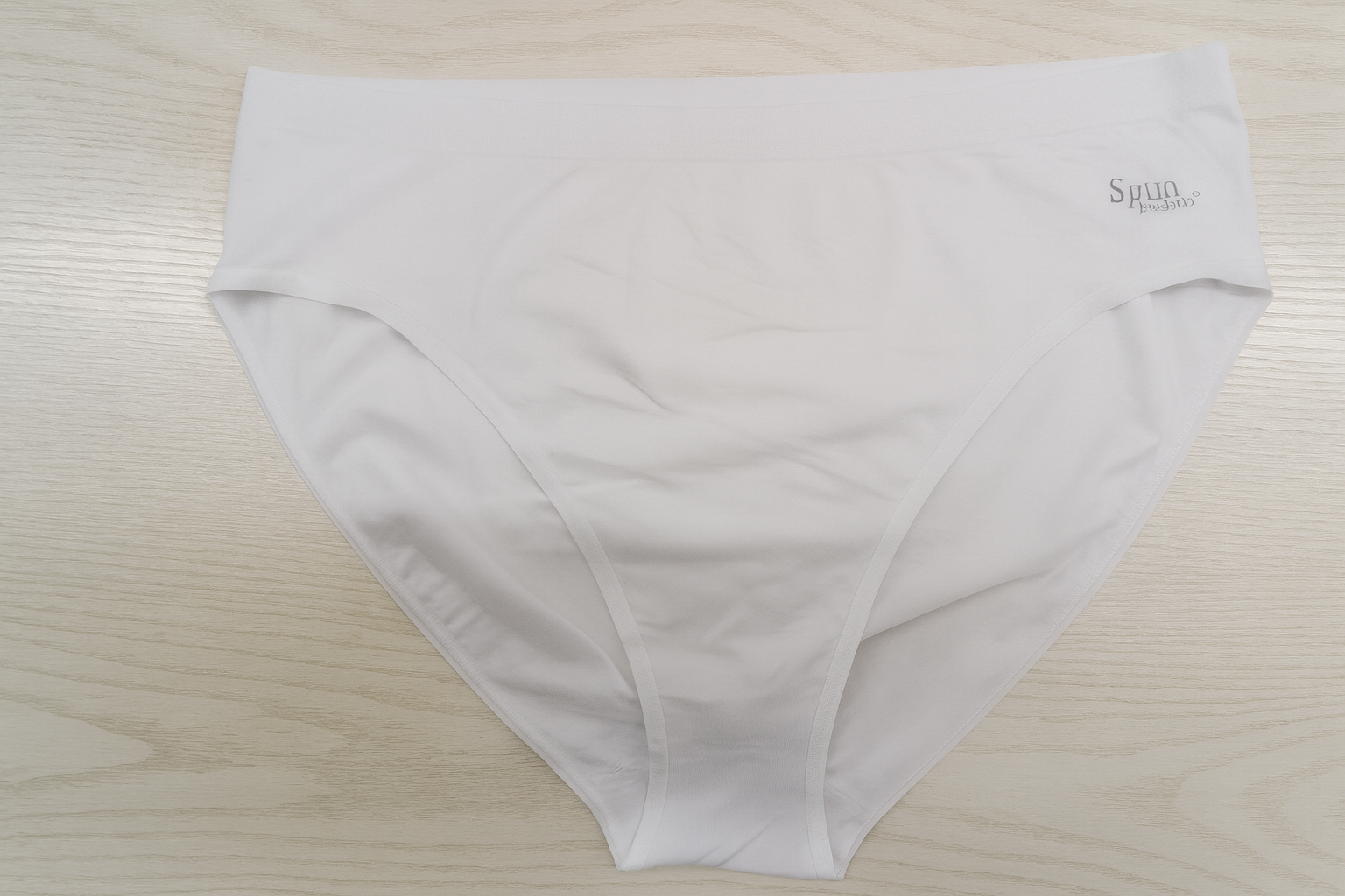 White underwear with a brand logo on a light wooden surface
