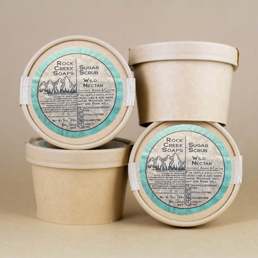 Three containers of Rock Creek Soaps Sugar Scrub on a beige background